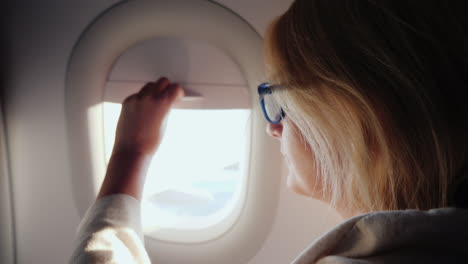 A-Woman-Opens-The-Porthole-Curtain-And-Looks-Out-The-Window-Of-The-Plane