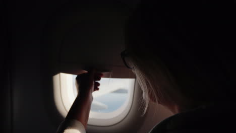 A-Woman-Opens-The-Porthole-Curtain-And-Looks-Out-The-Window-Of-The-Plane