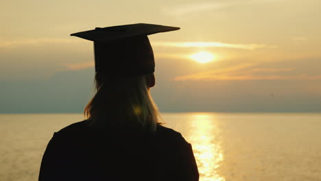 A-Bachelor-With-A-Diploma-In-Hand-And-A-Cap-Of-A-Graduate-Looks-At-The-Sunrise-Over-The-Sea