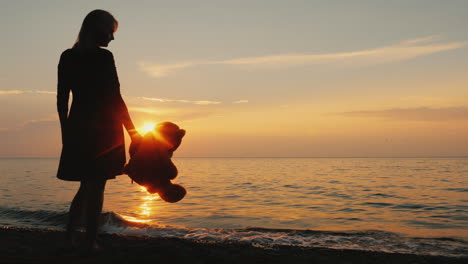 A-Woman-With-A-Teddy-Bear-In-Hand-Is-Standing-On-The-Seashore-When-The-Sun-Sets-Childhood-Dreams