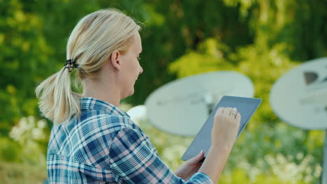 Woman-Tunes-Satellite-Dishes-Outdoors-Uses-Tablet