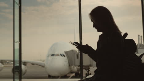 Silhouette-Of-A-Woman-With-Boarding-Documents-Standing-At-The-Terminal-Window-Outside-The-Window-A-B