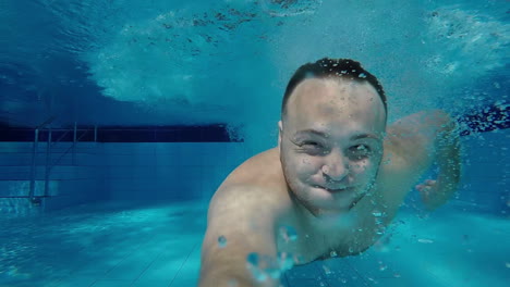 A-Man-Swims-Under-The-Water-In-The-Pool-With-His-Eyes-Open-Looking-Into-The-Camera-Underwater-Selfie