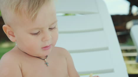 A-Boy-Of-1-Year-Eats-Cookies-Sits-On-A-White-Sunbed-On-The-Beach-Rest-On-The-Sea-With-A-Small-Child-