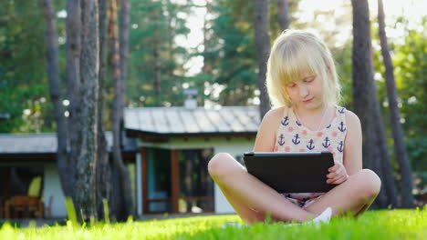The-Girl-Is-Playing-On-The-Tablet-The-Sun-Beautifully-Highlights-Her-Blond-Hair-Sits-On-The-Lawn-Nea