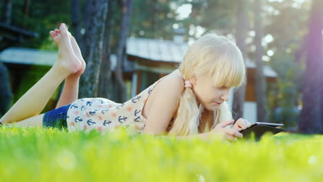 Blonde-Girl-6-Years-Playing-On-The-Tablet-Emotionally-Reacts-Lying-On-The-Lawn-In-The-Backyard-Of-Th