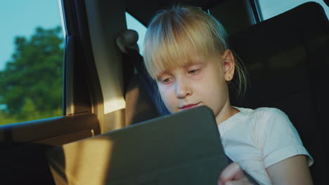 Caucasian-Girl-6-Years-Riding-In-The-Back-Seat-Of-The-Car-Playing-On-The-Tablet-Traveling-With-A-Chi
