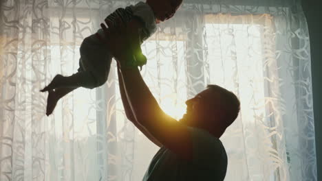 Silhouettes-Of-Loving-Parents-With-A-Child-At-The-Window-Of-Their-Apartment