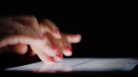 Female-Fingers-With-Red-Manicure-On-Their-Nails-Print-Text-On-The-Tablet-At-Night-Close-Up-4k-Video