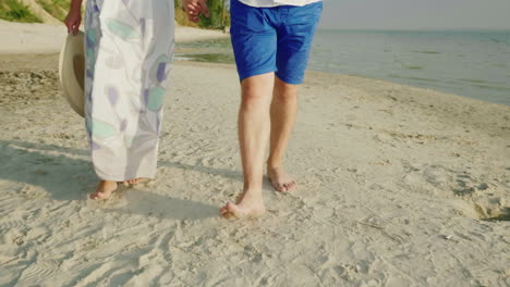 A-Young-Couple-Is-Walking-Barefoot-On-The-Sand-On-The-Beach-In-The-Frame-Only-The-Legs-Are-Visible-V