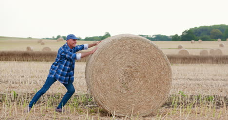 Farmer-Struggling-While-Rolling-Hay-Bale-At-Farm-1