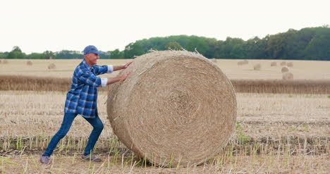 Farmer-Struggling-While-Rolling-Hay-Bale-At-Farm-3