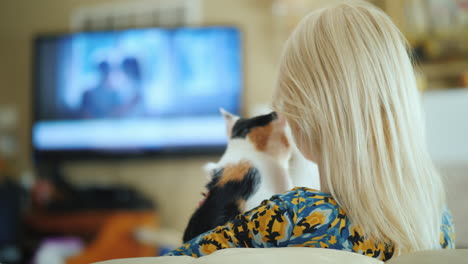 Blonde-Woman-With-A-Kitten-In-Her-Arms-Is-Watching-Tv-Rear-View