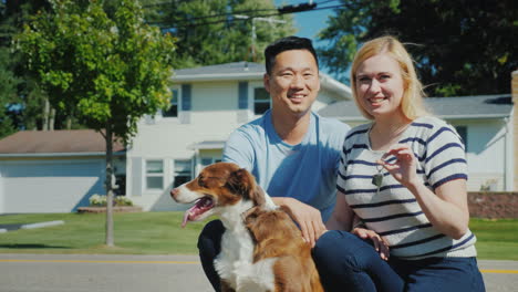 Happy-Multi-Ethnic-Family-With-A-Dog-Against-The-Background-Of-A-New-Home-Holds-The-Key-In-His-Hand