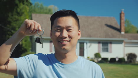 Portrait-Of-A-Young-Asian-Man-With-A-House-Key-In-His-Hand-Looking-At-The-Camera-Against-The-Backgro