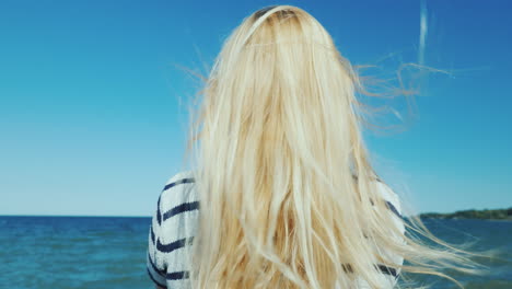 Blonde-Woman-With-Long-Hair-Looks-At-The-Sea-Wind-Ruffles-Her-Hair
