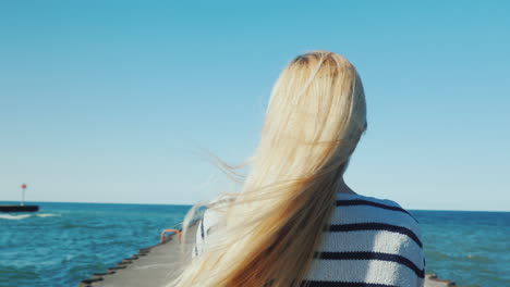 A-Woman-With-Long-Hair-Strolls-Along-The-Pier-The-Wind-Ruffles-Her-Hair-Back-View