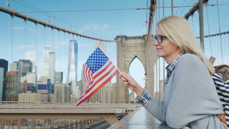 A-Woman-With-The-Flag-Of-America-In-Her-Hand-Stands-On-The-Brooklyn-Bridge-With-A-View-Of-Manhattan-