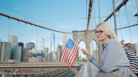 A-Woman-With-The-Flag-Of-America-In-Her-Hand-Stands-On-The-Brooklyn-Bridge-With-A-View-Of-Manhattan-