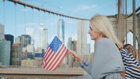 Young-Tourist-With-A-Flag-Of-America-And-A-Backpack-Standing-On-The-Brooklyn-Bridge-On-The-Backgroun