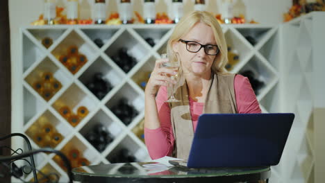 Woman-Tasting-Wine-Sitting-At-A-Table-In-A-Winery-Using-A-Laptop
