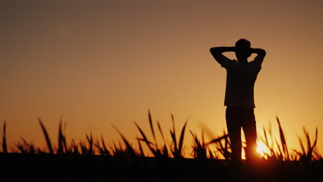 Silhouette-A-Young-Man-Enjoys-The-Fresh-Air-And-Admires-The-Sunset-He-Holds-His-Hands-Behind-The-Bac