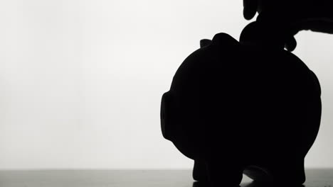 Silhouette-Of-A-Hand-That-Throws-Coins-Into-A-Piggy-Bank-On-A-White-Background-4K-Video