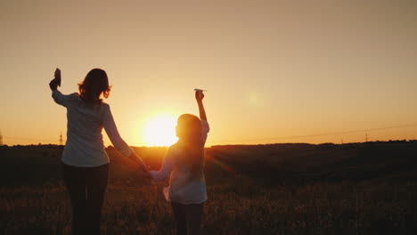 Mom-And-Daughter-Are-Playing-Paper-Airplanes-At-Sunset-In-A-Picturesque-Place-Happy-Time-With-The-Ba