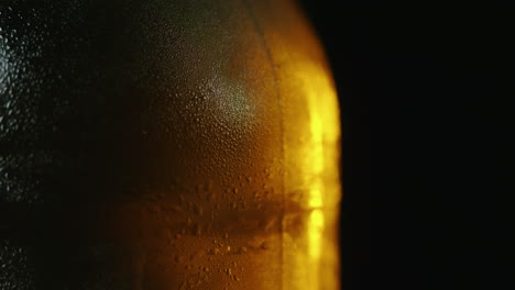 Eine-Flasche-Kaltes-Bier-Mit-Wassertröpfchen-Dreht-Sich-Langsam-Und-Wird-Von-Einem-Lichtstrahl-Auf-Einem-Bl-Beleuchtet