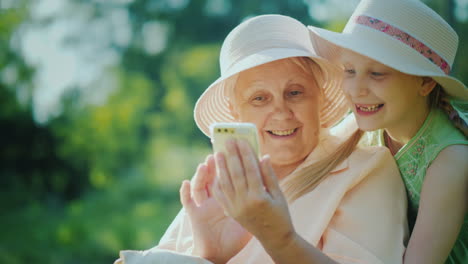 Happy-Girl-With-Grandmother-Looking-At-The-Smartphone-Screen-Together-Have-A-Rest-Together-In-A-Summ