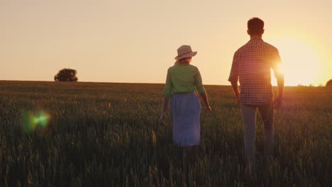 Two-Young-Farmer-Man-And-Woman-Are-Walking-Along-The-Wheat-Field-At-Sunset-Organic-Farmer-Concept-4K