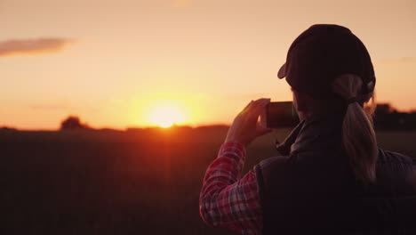 Junge-Bäuerin-Fotografiert-Einen-Wunderschönen-Sonnenuntergang-über-Einem-Weizenfeld-4k-Video