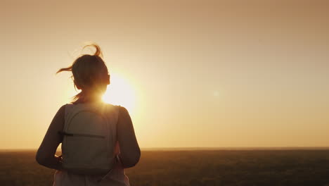 A-Young-Woman-With-A-Backpack-Runs-Forward-Towards-The-Sun-Hair-Glows-In-The-Rays-Of-Sunset-Slow-Mot