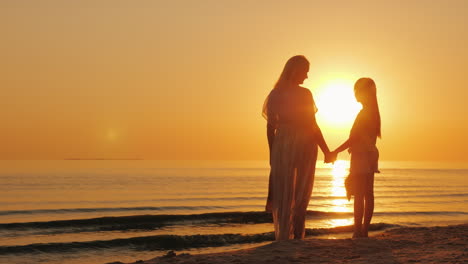 Mom-And-Daughter-Are-Looking-Forward-To-A-Beautiful-Sunset-Over-The-Sea-Silhouettes-Of-A-Woman-With-