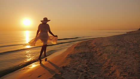 A-Woman-In-A-Light-Couple-Walks-Along-The-Beach-At-Sunset-Carefree-And-Cheerful-Woman