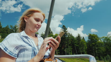 A-Woman-Uses-A-Smartphone-Rides-In-The-Open-Cabin-Of-The-Cable-Car-On-Vacation-In-Connection-With-Th