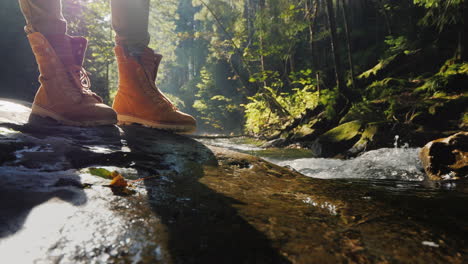 The-Feet-Of-The-Traveler-Stand-On-A-Wet-Log-Near-A-Mountain-Stream-Tourism-And-Hiking-Conceptt