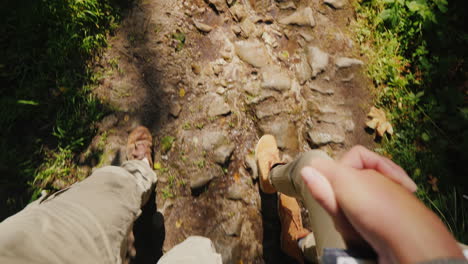 A-Couple-Of-Tourists-Hold-Hands-And-Walk-On-A-Slippery-Stony-Path-In-The-Forest-Only-The-Legs-Are-Vi