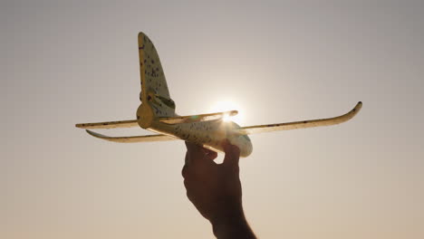 Hand-With-A-Toy-Airplane-On-A-Background-Of-Sky-And-Sun