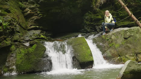 Eine-Frau-In-Einer-Gelben-Daunenjacke,-Die-Den-Wasserfall-Im-Wald-Bewundert-4k-Video
