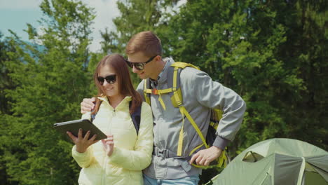 A-Young-Couple-Of-Tourists-Enjoy-A-Tablet-In-The-Camping-Stand-Near-The-Tent-Technology-On-Vacation-