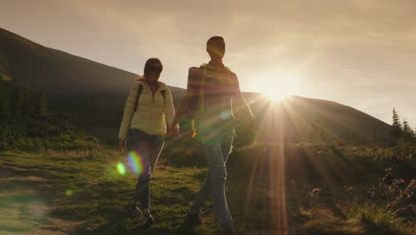 Young-Couple-Of-Tourists-Holding-Hands-Walking-Along-A-Mountain-Path-In-The-Rays-Of-The-Setting-Sun-