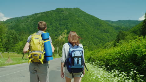 A-Young-Tourist-Couple-Walks-Along-The-Road-To-Beautiful-Mountains-Covered-With-Forest-Active-Way-Of