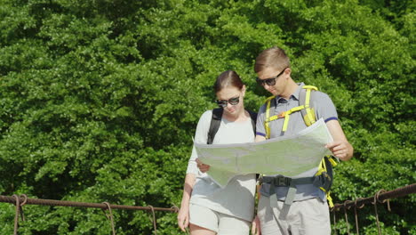 A-Man-And-A-Woman-Are-Studying-The-Map-They-Stand-On-The-Bridge-In-The-Background-Of-A-Picturesque-S
