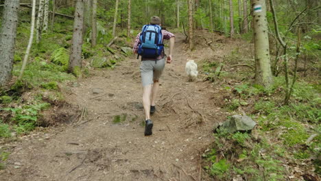 In-A-Hike-With-Your-Favorite-Dog-A-Man-With-A-Backpack-Runs-After-His-Pet-On-A-Forest-Path