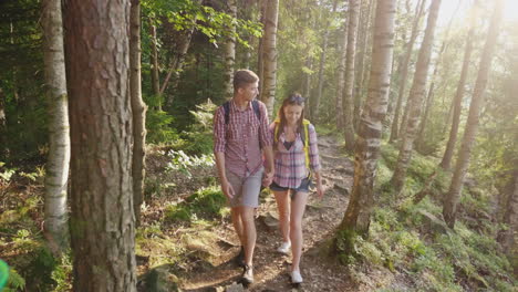 Young-Tourists-With-Backpacks-Walk-Along-A-Trail-In-The-Forest