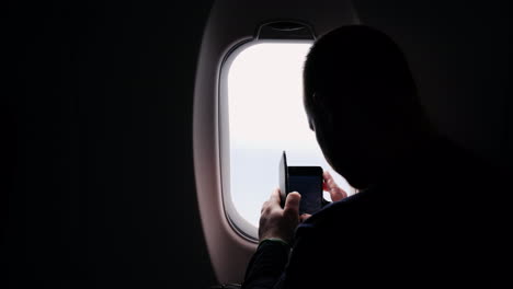 A-Silhouette-Of-A-Man-Taking-Pictures-Of-The-View-From-The-Plane-Window