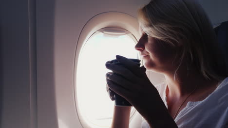 A-Woman-Is-Drinking-Coffee-In-The-Cabin-Of-An-Airplane-Sits-By-The-Window