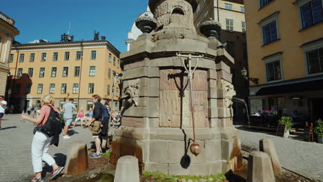 Fountain-With-Drinking-Water-In-The-Old-City-Of-Stockholm-Nearby-Tourists-Walk-A-Popular-Holiday-Des
