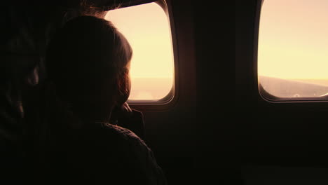 Girl-Sitting-In-An-Airplane-Looking-Out-The-Window-At-The-Rising-Sun